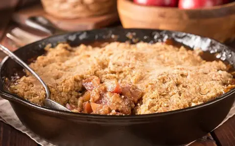Un délice de pâte à crumble croustillante sur un lit de fruits fondants, servi dans une poêle en fonte.