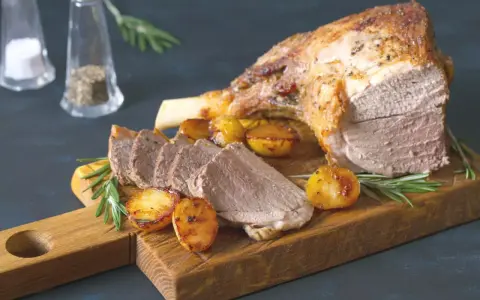 Un gigot de 7 heures, tendre et juteux, servi avec des pommes de terre rôties et du romarin sur une planche en bois.