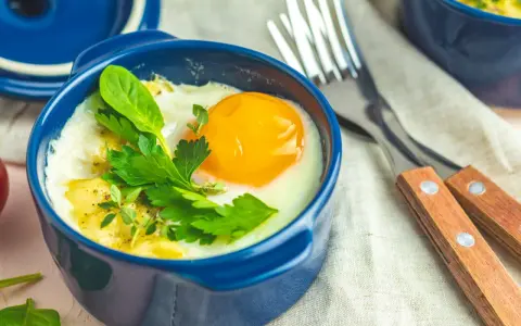 Un œuf cocotte appétissant dans un ramequin bleu, garni d'herbes fraîches. Un délice pour le petit-déjeuner.