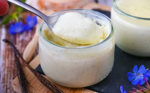 Délicieuse crème vanille recette, onctueuse et parsemée de grains de vanille, servie dans un pot en verre.