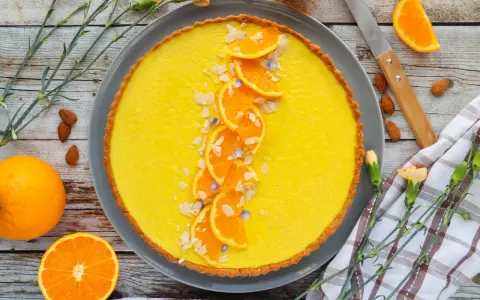Une délicieuse tarte à l'orange, garnie de fines tranches d'orange, d'amandes effilées et de petites fleurs bleues. Un régal visuel et gustatif.