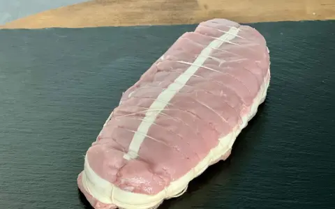 Rôti de veau cru ficelé, prêt à cuire, sur une planche sombre.