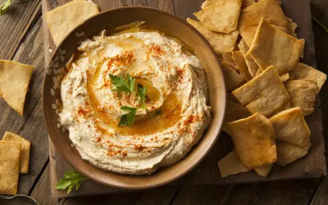 Houmous crémeux, garni de paprika et de persil, servi avec des chips pita croustillantes. Une recette houmous facile pour un apéritif gourmand.