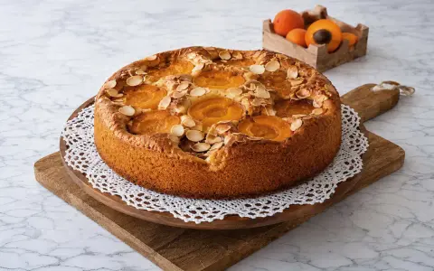 Un délicieux gâteau aux abricots, garni d'amandes effilées, est présenté sur une planche en bois.