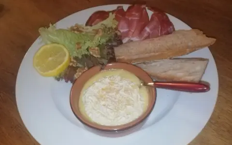 Un plat avec un fromage fondant, des tranches de jambon, de la salade, des noix, une tranche de citron et du pain. Une idée de recette amuse bouche facile sans cuisson.