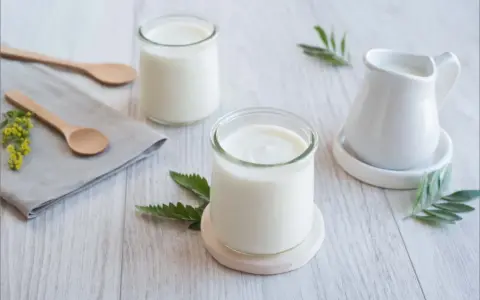 Deux pots de yaourt, une petite cruche et des cuillères en bois sur une table. La couleur blanche du lait, pourquoi est-il si pur ?