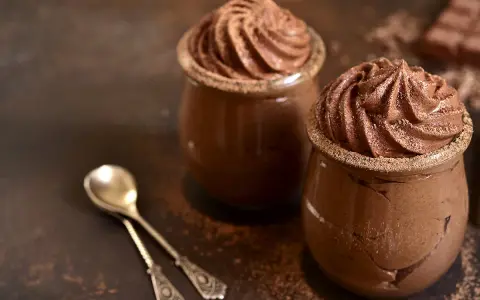 Deux pots de mousse au chocolat onctueuse, saupoudrés de cacao, avec deux cuillères argentées.