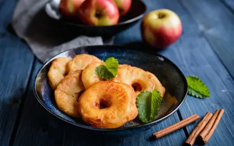 Délicieux beignets aux pommes dorés, garnis de menthe fraîche et accompagnés de bâtons de cannelle sur une table en bois bleu.