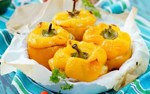 Quatre poivrons farcis jaunes, dorés et appétissants, servis dans un plat garni de papier sulfurisé et décorés de persil frais.