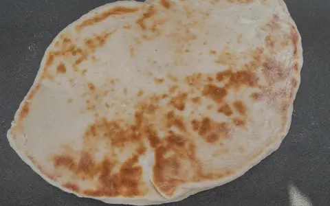 Un naan au fromage, peut-être avec un peu de La Vache qui rit, doré et moelleux, prêt à être dégusté.