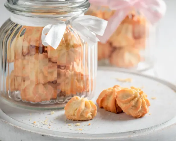Biscuits sablés dans des bocaux en verre décorés de rubans blancs et roses, parfaits pour un dessert pique-nique.