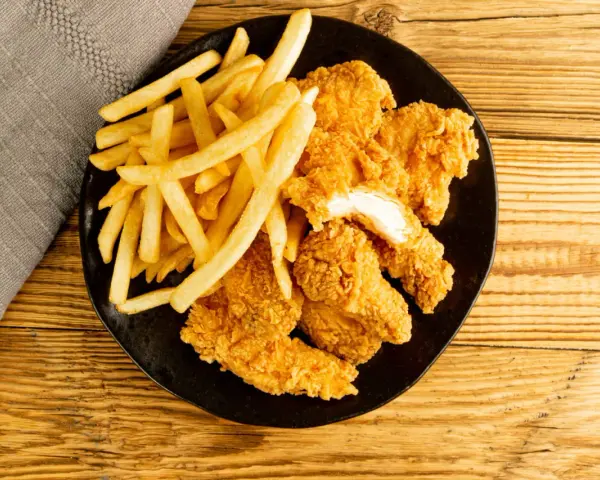Assiette de nuggets maison dorés et croustillants avec des frites, sur fond de bois.