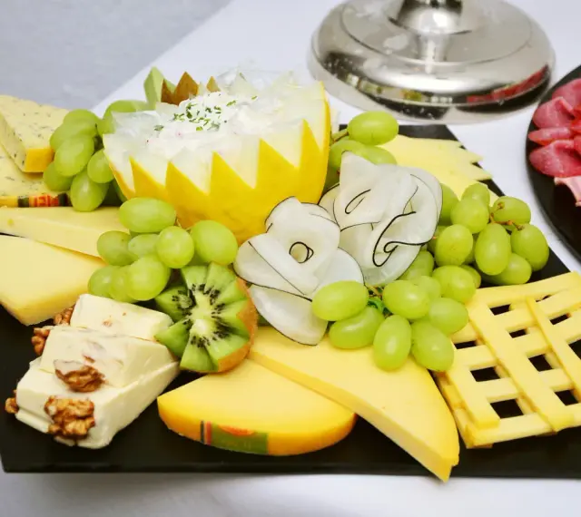 Plateau de fromage festif avec raisins verts, kiwi, noix et charcuterie. Une belle décoration plateau de fromage pour un événement.