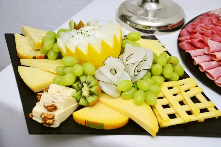 Plateau de fromage festif avec raisins verts, kiwi, noix et charcuterie. Une belle décoration plateau de fromage pour un événement.