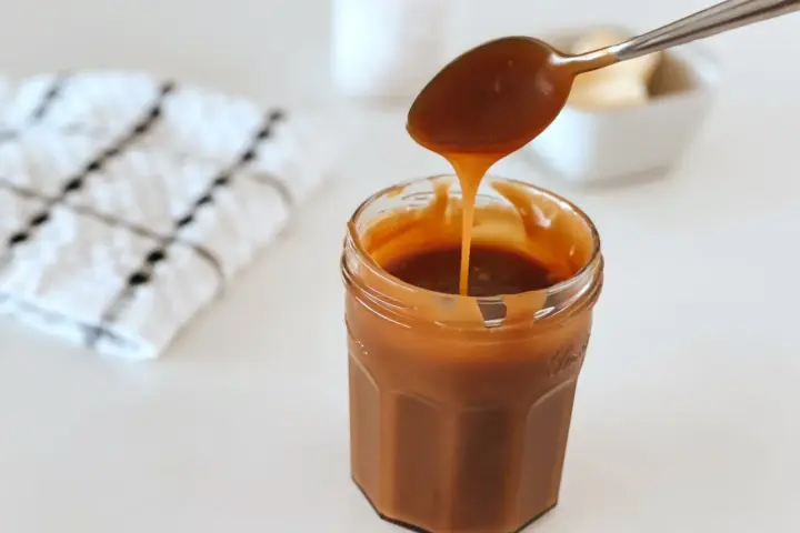 Une cuillère verse du caramel onctueux dans un pot. La recette caramel parfaite pour vos desserts.