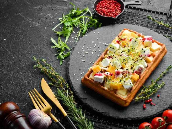 Gaufre rectangulaire garnie de dés de fromage, de fruits et de pousses, servie sur une ardoise. Une délicieuse pâte à gaufre salée prête à être dégustée.