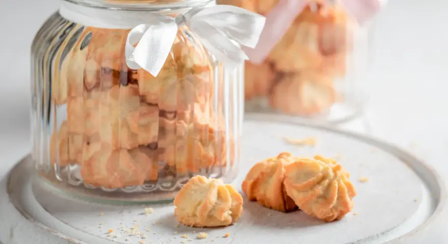 Biscuits sablés dans des bocaux en verre décorés de rubans blancs et roses, parfaits pour un dessert pique-nique.