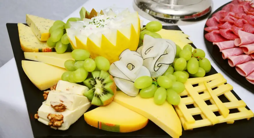 Plateau de fromage festif avec raisins verts, kiwi, noix et charcuterie. Une belle décoration plateau de fromage pour un événement.