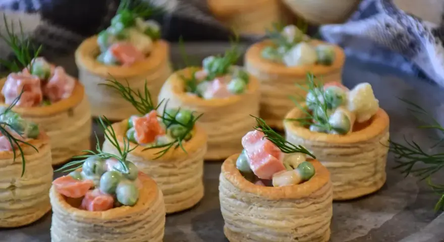 Petits bouchées à la reine, garnies d'une salade crémeuse de petits pois, carottes et jambon, décorées d'aneth. Parfaites pour un apéritif gourmand.