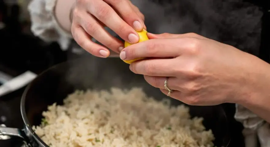 Des mains pressent un citron sur une soupe de riz fumante, ajoutant une touche de fraîcheur à ce plat réconfortant.