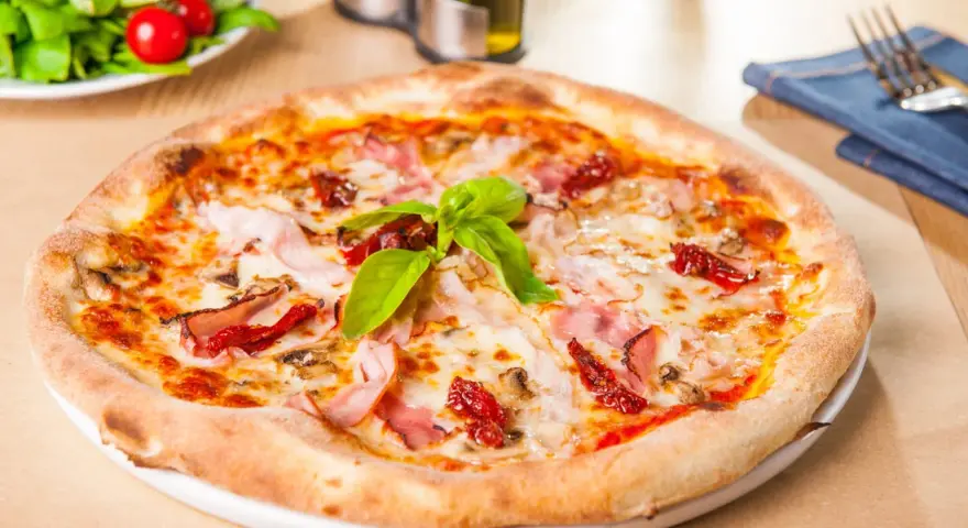 Pizza garnie de jambon, tomates séchées et champignons, parfaite pour une recette pâte à pizza rapide. Une salade fraîche est servie à côté.