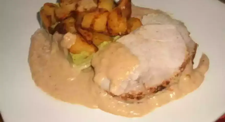 Tranche de roti de porc au lait, nappée d'une sauce onctueuse, accompagnée de pommes de terre rôties croustillantes. Un plat réconfortant.