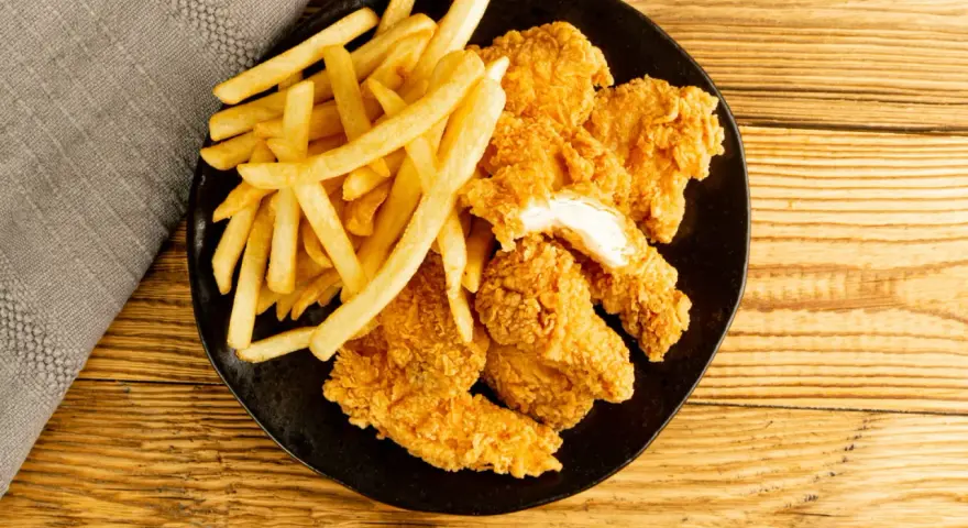 Assiette de nuggets maison dorés et croustillants avec des frites, sur fond de bois.