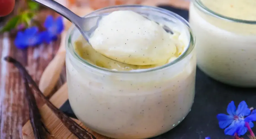 Délicieuse crème vanille recette, onctueuse et parsemée de grains de vanille, servie dans un pot en verre.