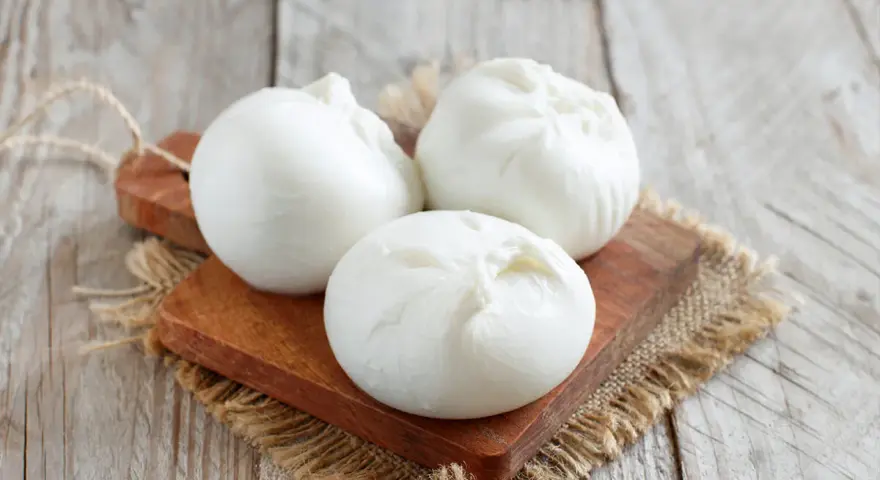 Trois boules de burrata crémeuse sur une planche en bois, parfaites pour comprendre la différence burrata et mozzarella.