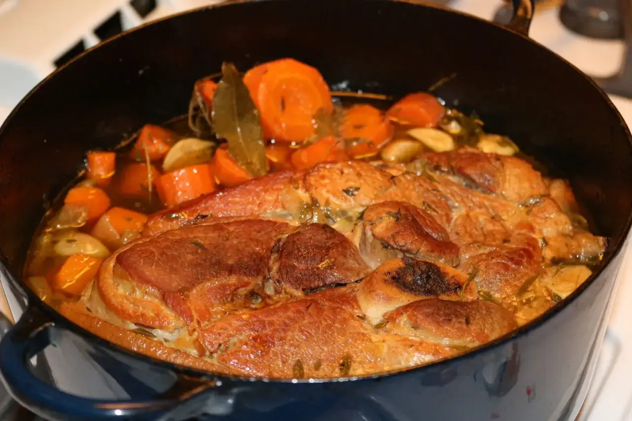 Rouelle de porc fondante mijotant avec des carottes et des herbes dans une cocotte. Un délice à savourer !