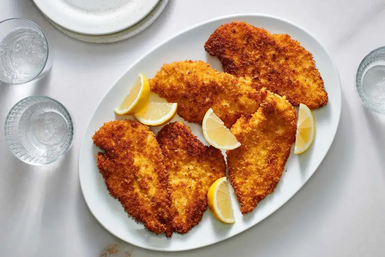 Cinq morceaux de poulet pané dorés et croustillants, servis sur une assiette blanche avec des quartiers de citron. Un délice à paner !