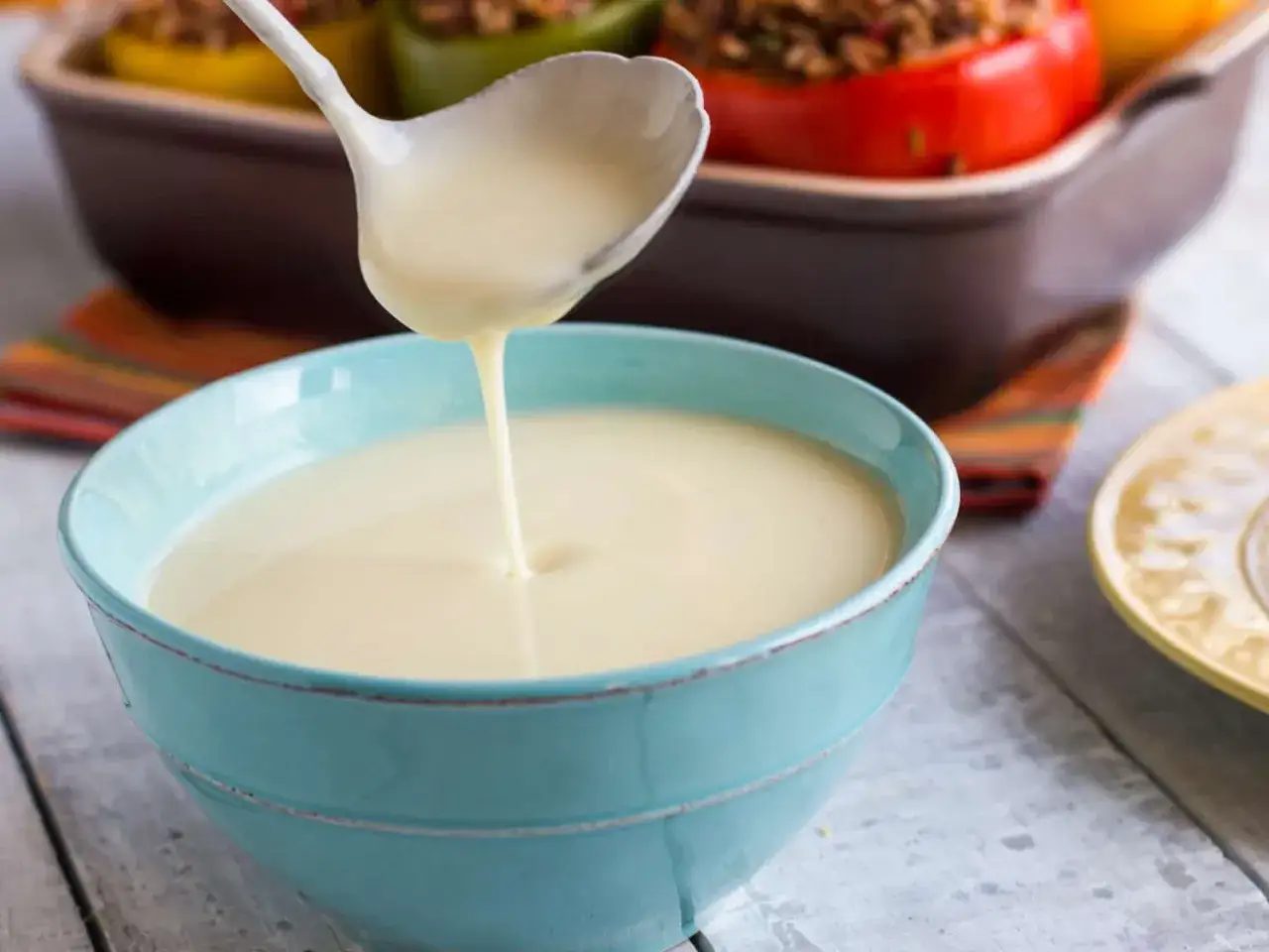 Une louche verse une sauce onctueuse dans un bol bleu. Parfait pour accompagner des poivrons farcis.
