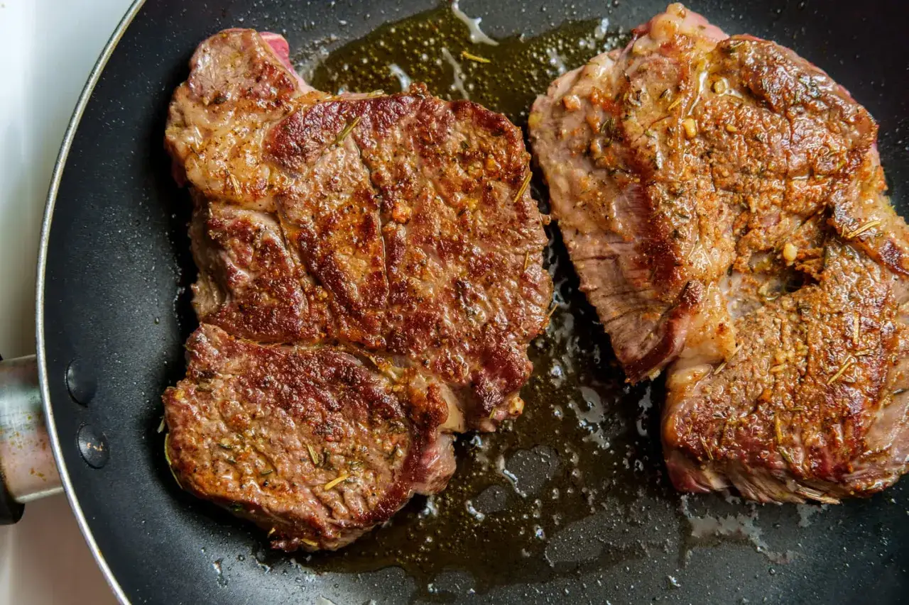 Deux belles côtes de porc, dorées et juteuses, mijotent dans une poêle avec des herbes aromatiques.