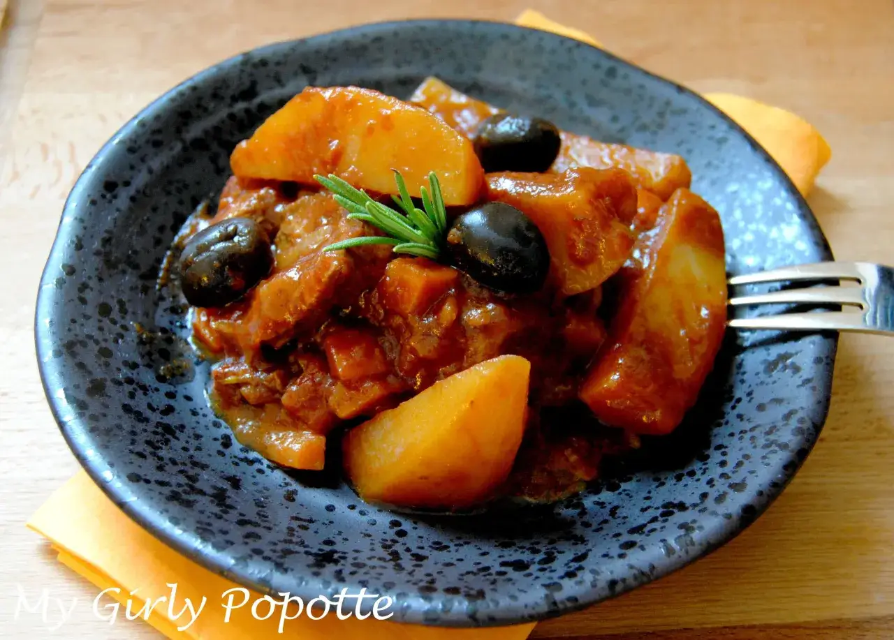 Un savoureux sauté de veau tomates champignons, garni d'olives noires et d'une touche de romarin, servi dans une assiette sombre.