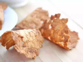 Trois tuiles aux amandes croustillantes, dorées et délicates, posées sur une planche en bois.