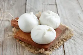 Trois boules de burrata crémeuse sur une planche en bois, parfaites pour comprendre la différence burrata et mozzarella.