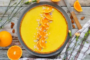 Une délicieuse tarte à l'orange, garnie de fines tranches d'orange, d'amandes effilées et de petites fleurs bleues. Un régal visuel et gustatif.