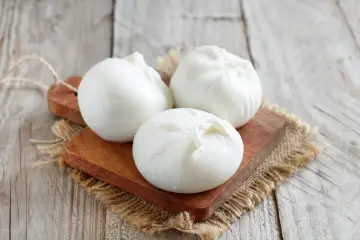 Trois boules de burrata crémeuse sur une planche en bois, parfaites pour comprendre la différence burrata et mozzarella.