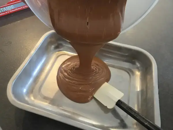 Comment faire une ganache : du chocolat fondu coule d'un bol dans un plat, guidé par une spatule.