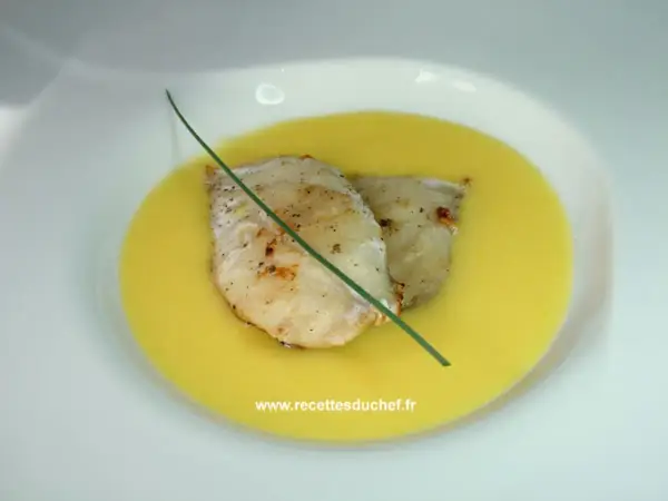 Deux filets de poisson poêlés reposent dans une onctueuse sauce à l'orange, décorés d'une tige de ciboulette.