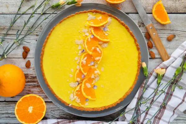 Une délicieuse tarte à l'orange, garnie de fines tranches d'orange, d'amandes effilées et de petites fleurs bleues. Un régal visuel et gustatif.