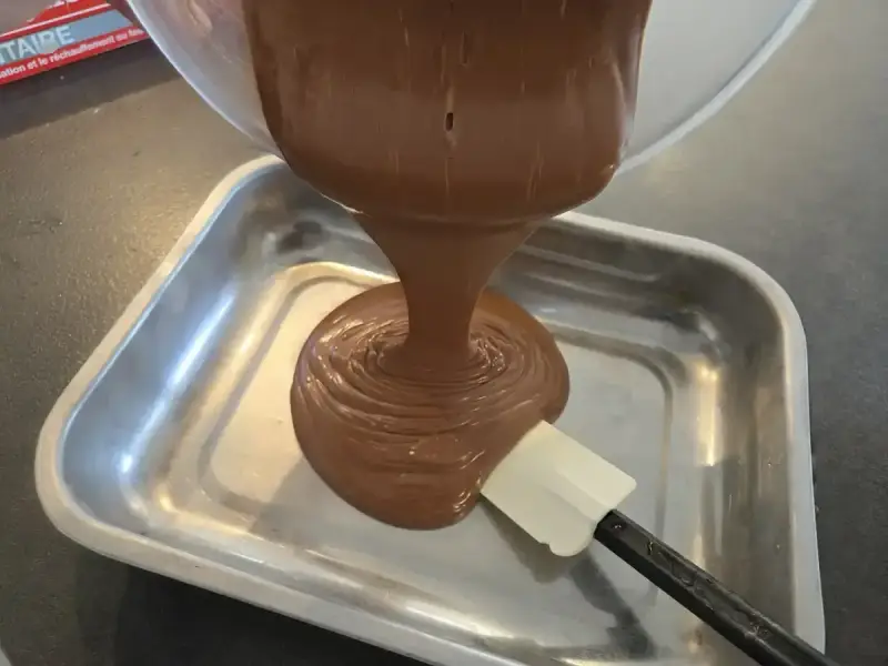 Comment faire une ganache : du chocolat fondu coule d'un bol dans un plat, guidé par une spatule.