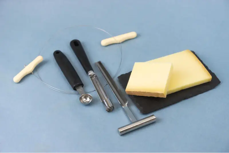 Des morceaux de fromage, des outils pour le découper et une ficelle. L'origine du fromage la dent du chat est un mystère savoureux.