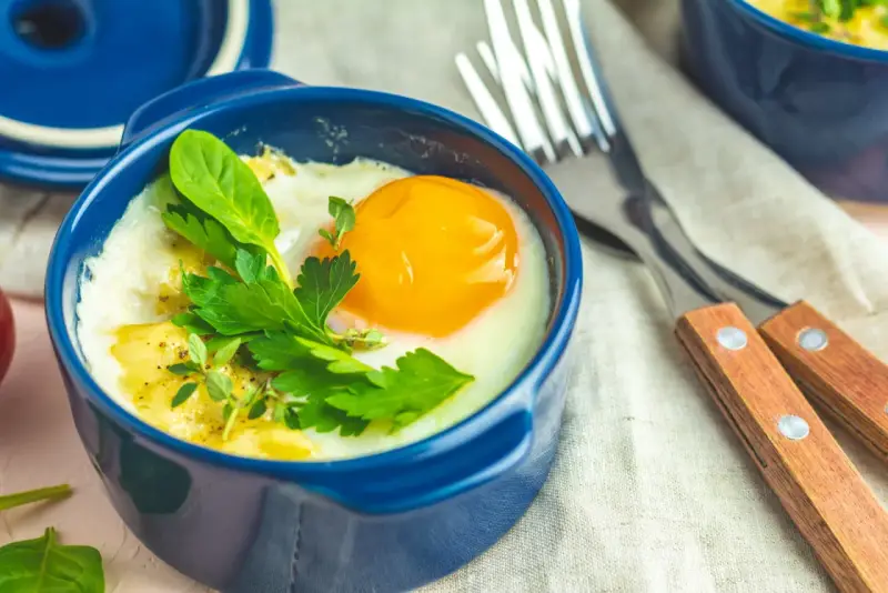 Un œuf cocotte appétissant dans un ramequin bleu, garni d'herbes fraîches. Un délice pour le petit-déjeuner.