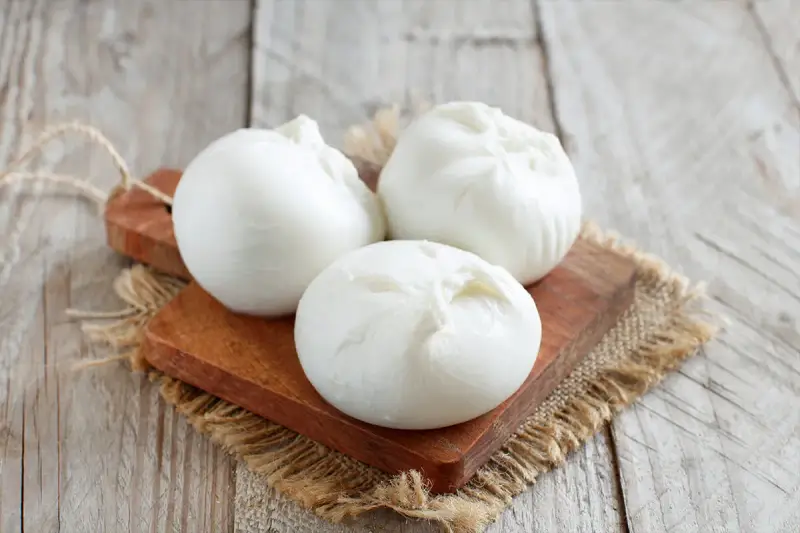 Trois boules de burrata crémeuse sur une planche en bois, parfaites pour comprendre la différence burrata et mozzarella.